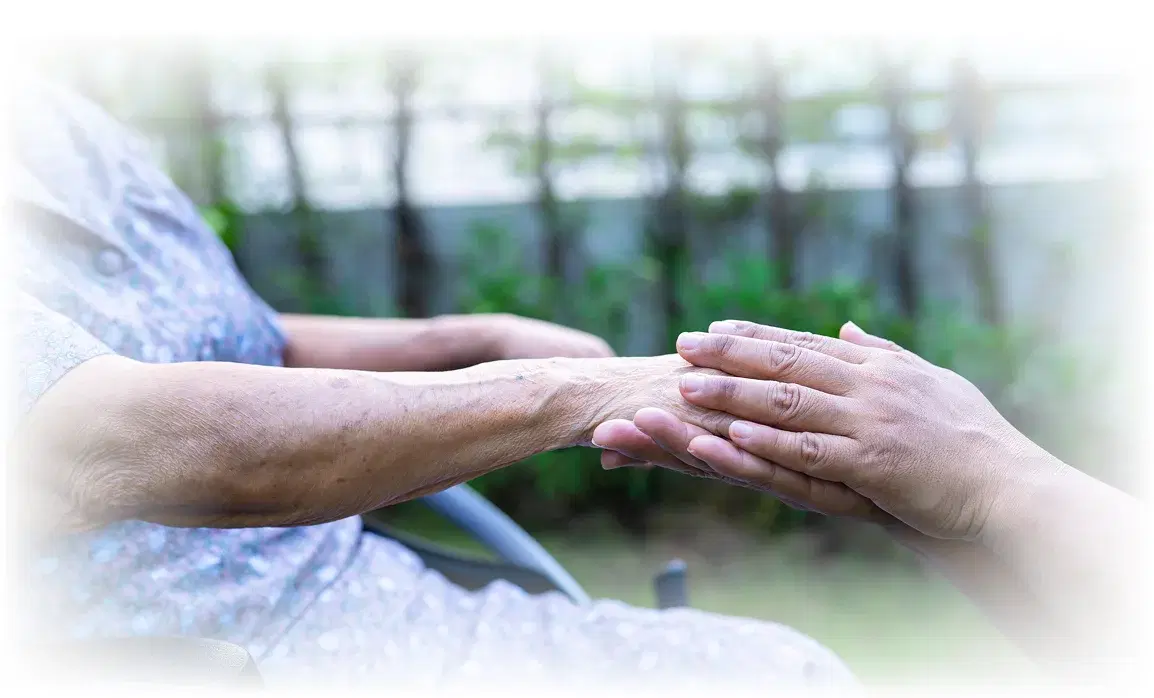 A caregiver holding an elderly patient's hand at home.