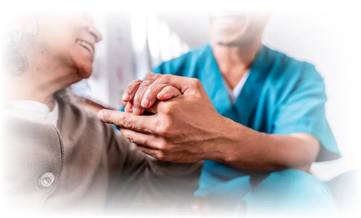 A nurse in teal scrubs holding hands with a smiling elderly patient.