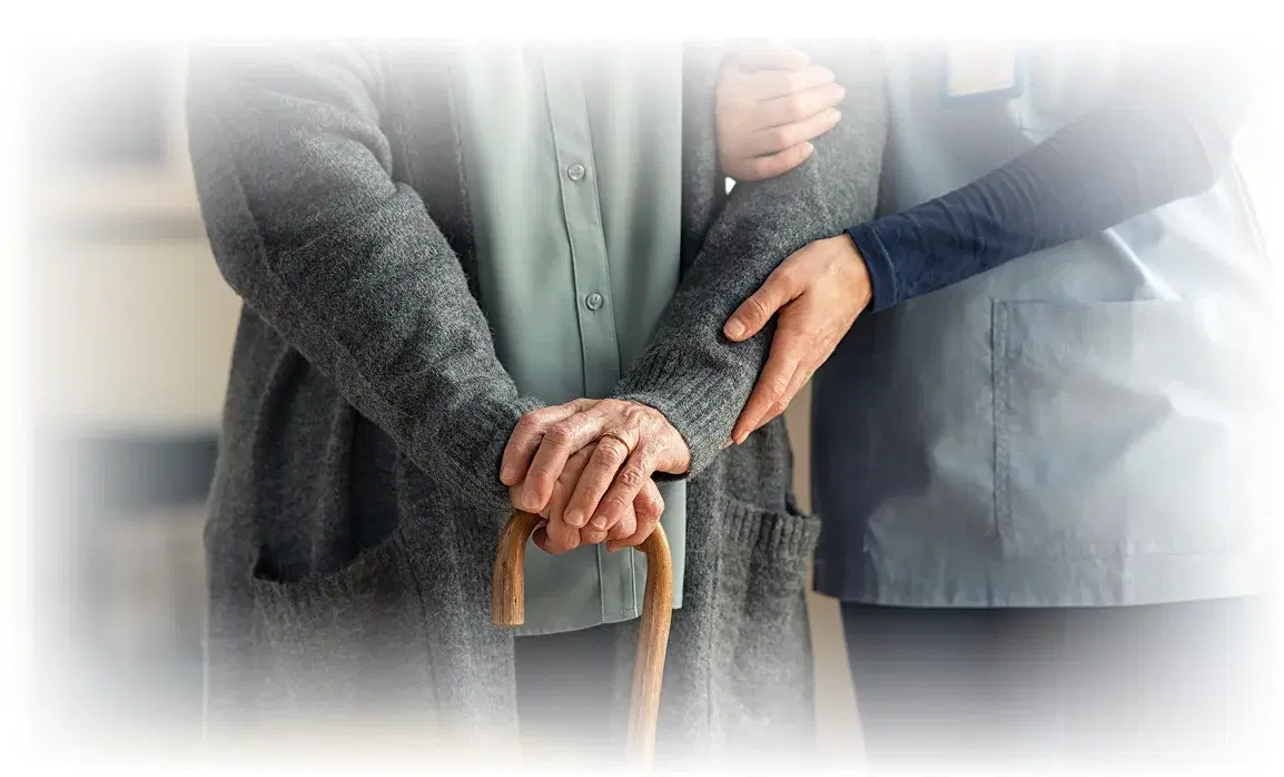 A nurse in teal scrubs holding hands with a smiling elderly patient.