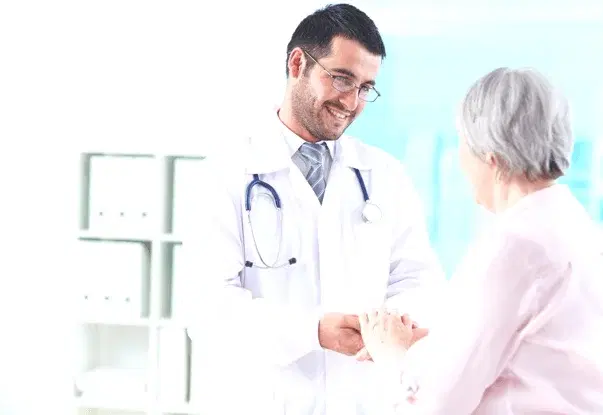 A doctor warmly holding an elderly patient's hand during a consultation.